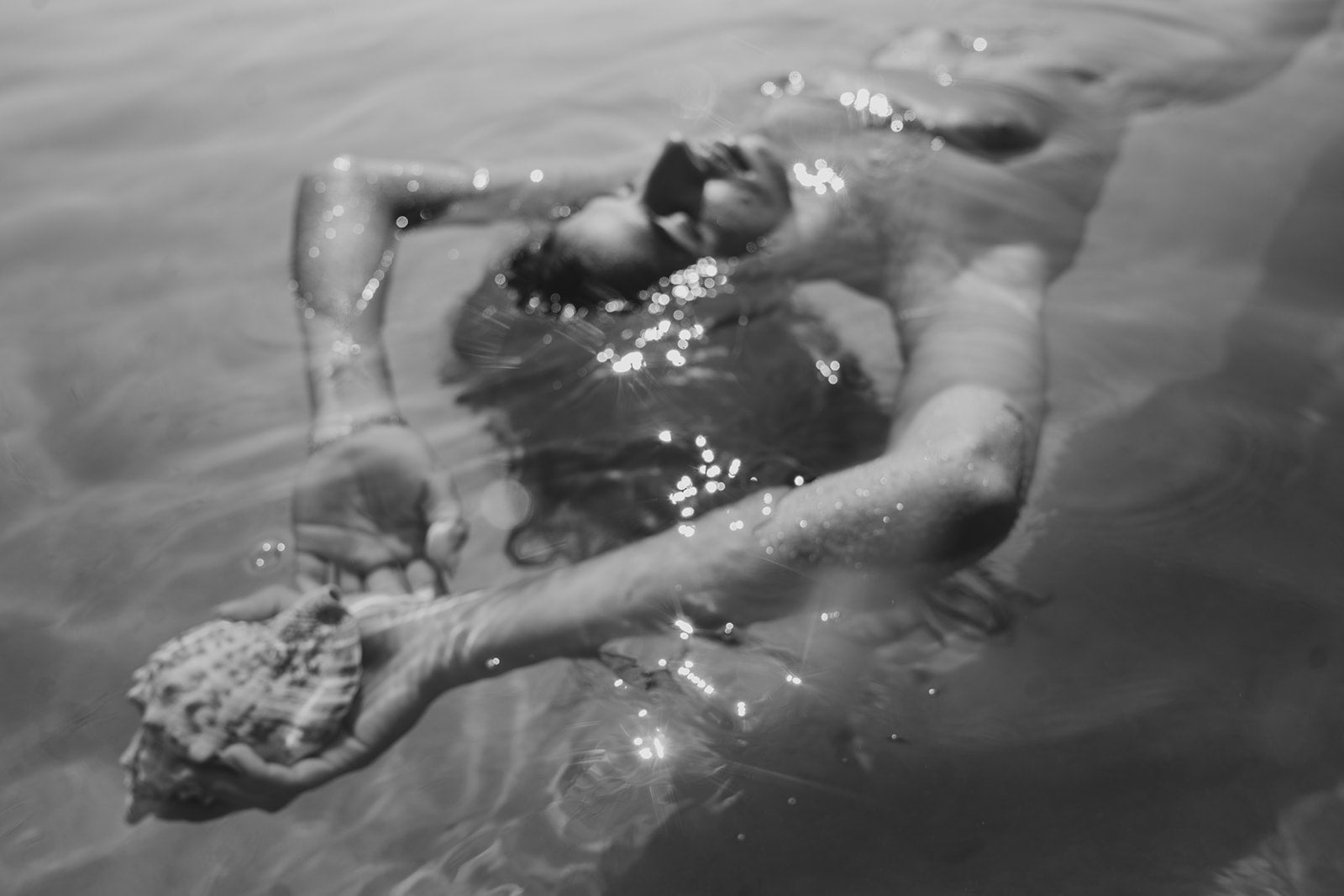 Person floating calmly in water holding a seashell, evoking balance, light exposure, and the relationship between environment, skin, and overall skin longevity.
