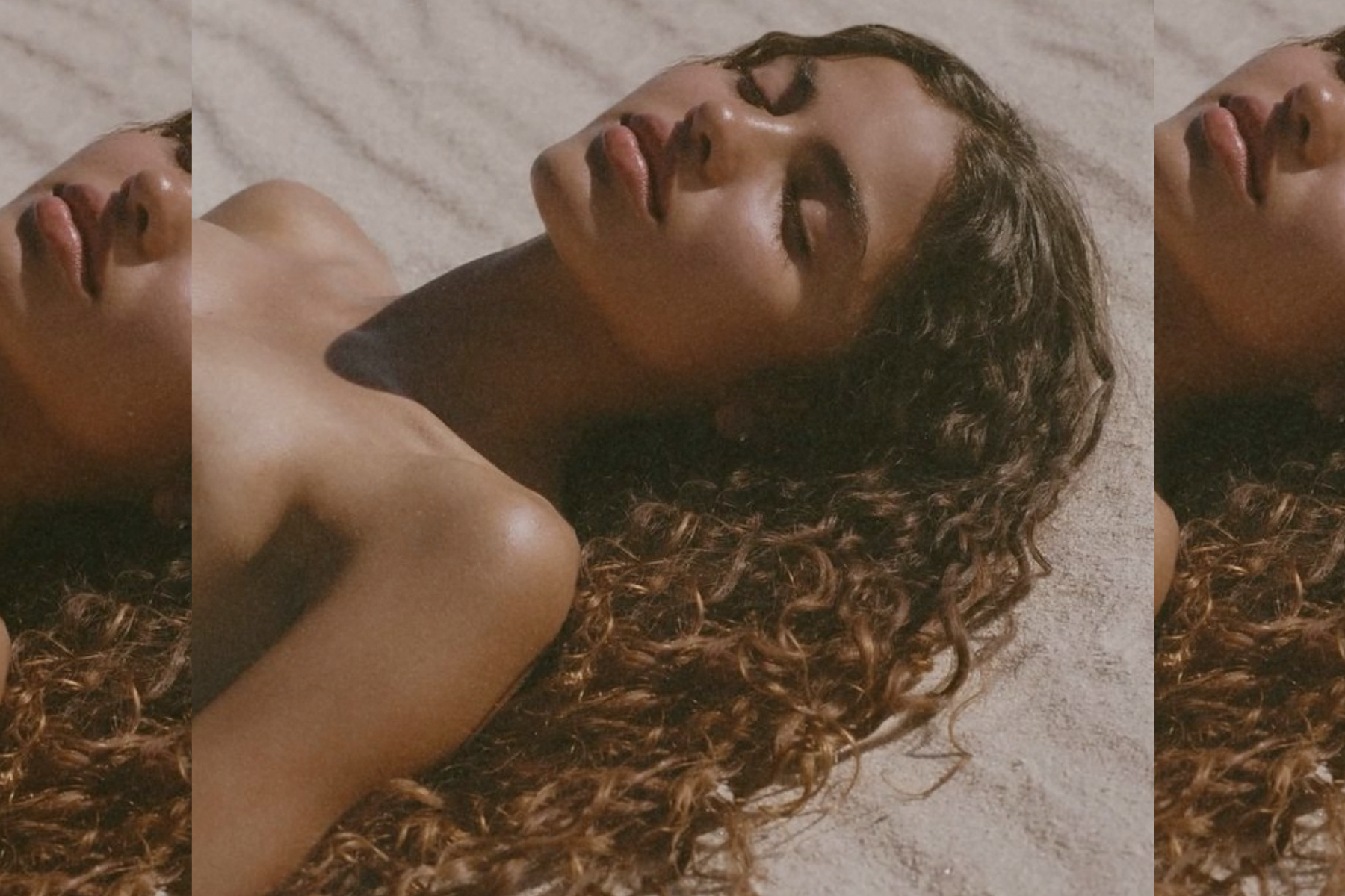 Woman lying on stone with eyes closed, skin illuminated by sunlight, hair spread naturally, conveying warmth, stillness, and ease.