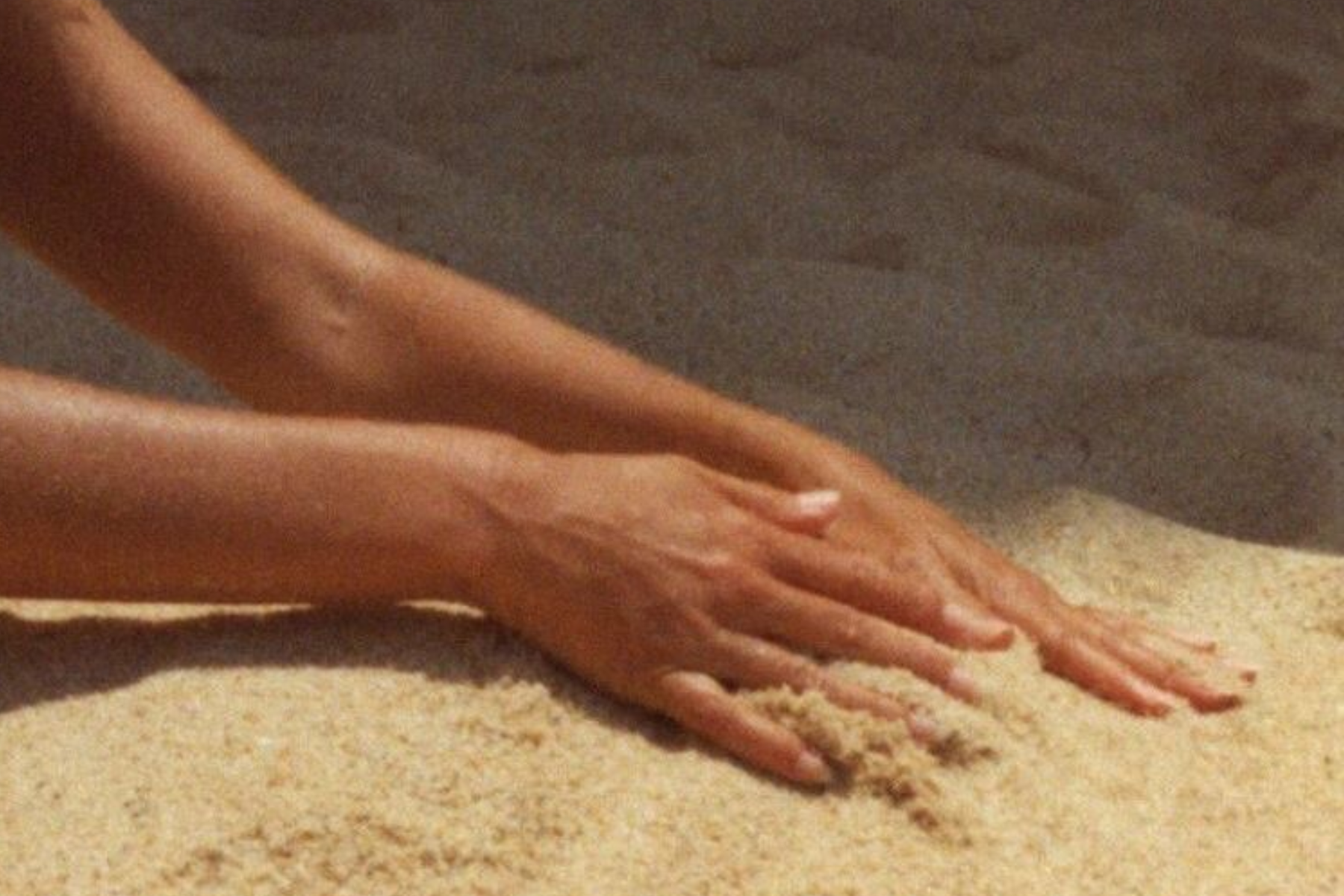Close-up of a person’s hands touching sand on the ground