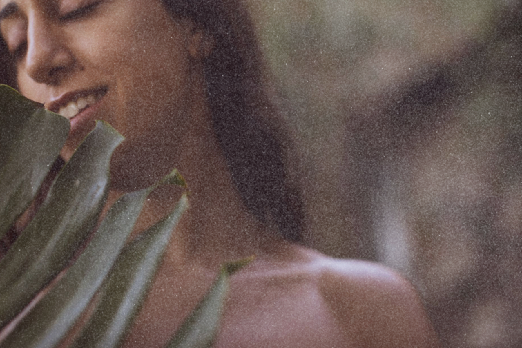 Close-up of a person smiling outdoors, partially obscured by a large green leaf.