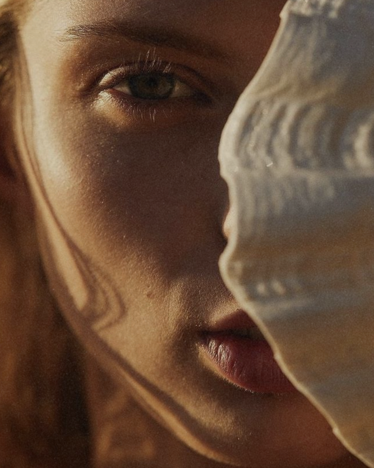 Close-up portrait of a woman in natural light with a seashell partially covering her face, used to introduce a section explaining how internal skin nutrition works beneath the surface before visible changes appear.