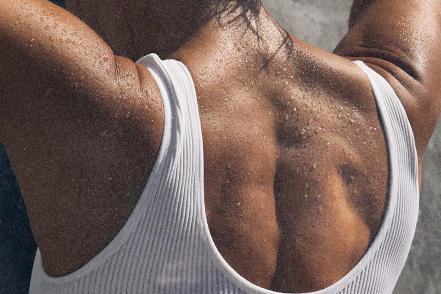 Close-up of a person’s upper back and shoulders in a tank top, with water droplets on the skin.