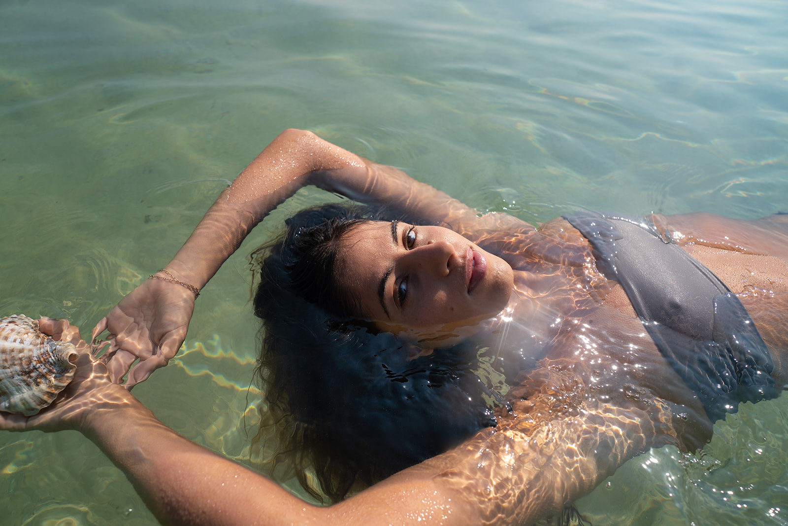 Woman floating in clear water with sunlight reflecting across her skin.