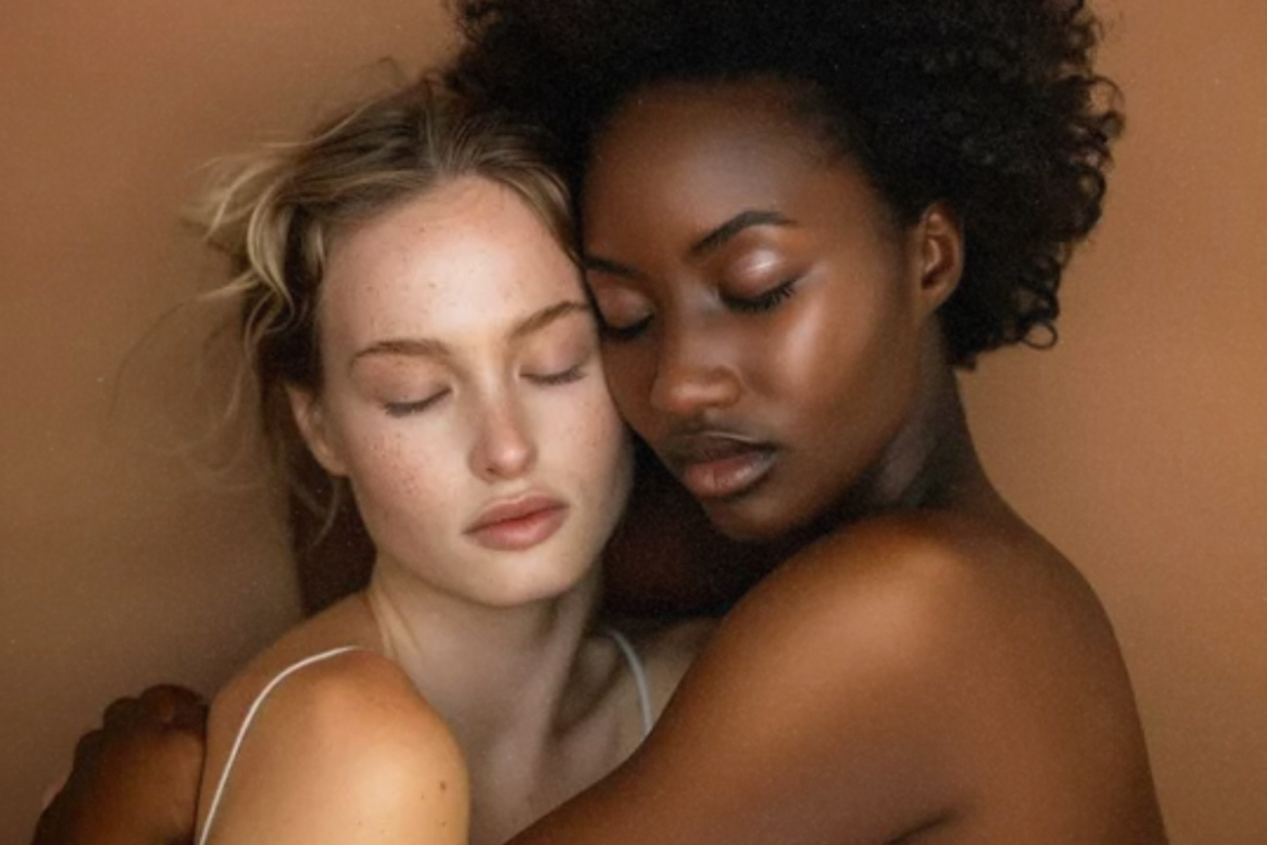 Two women with different skin tones embracing gently with eyes closed.