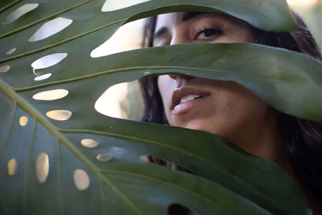 Marine vs. Bovine Collagen by ATIKA — A woman’s face half-covered by a large leaf, symbolizing natural beauty and the balance between marine and bovine collagen sources.