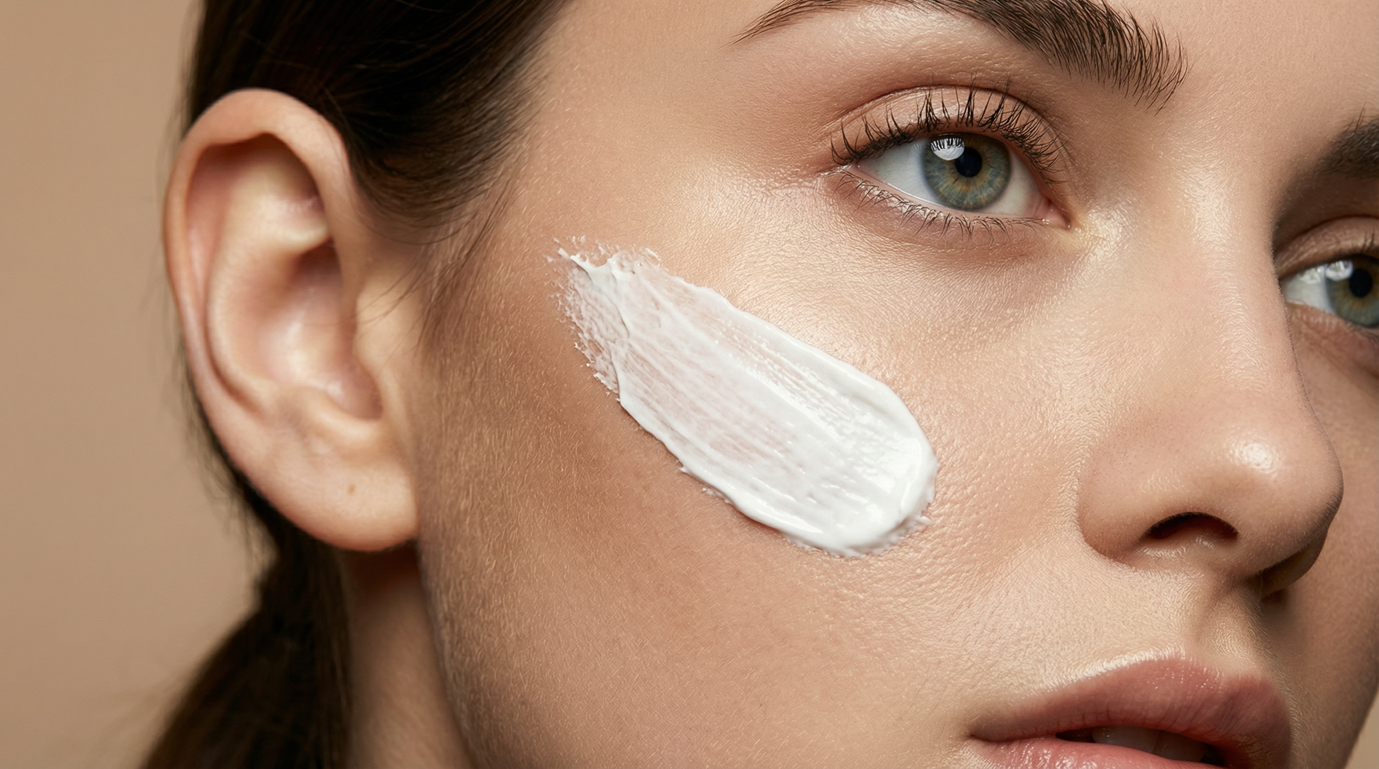 Woman applying sunscreen to her cheek, showing a visible streak of white sunscreen on the skin.