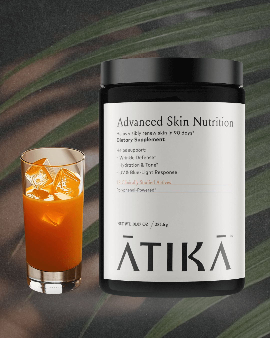 ATIKA Advanced Skin Nutrition jar beside a glass of orange-colored drink on a dark leafy background